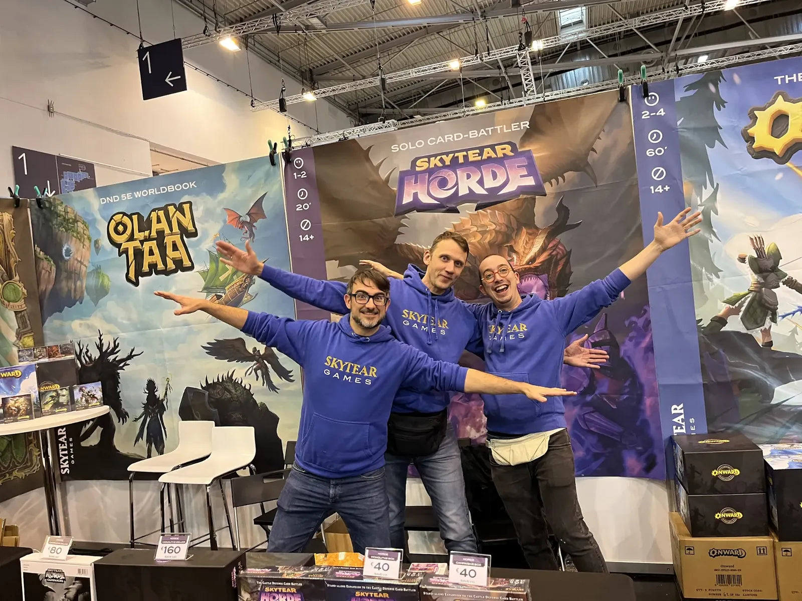 Three of the Skytear team in matching blue hoodies, arms spread wide, at our convention booth